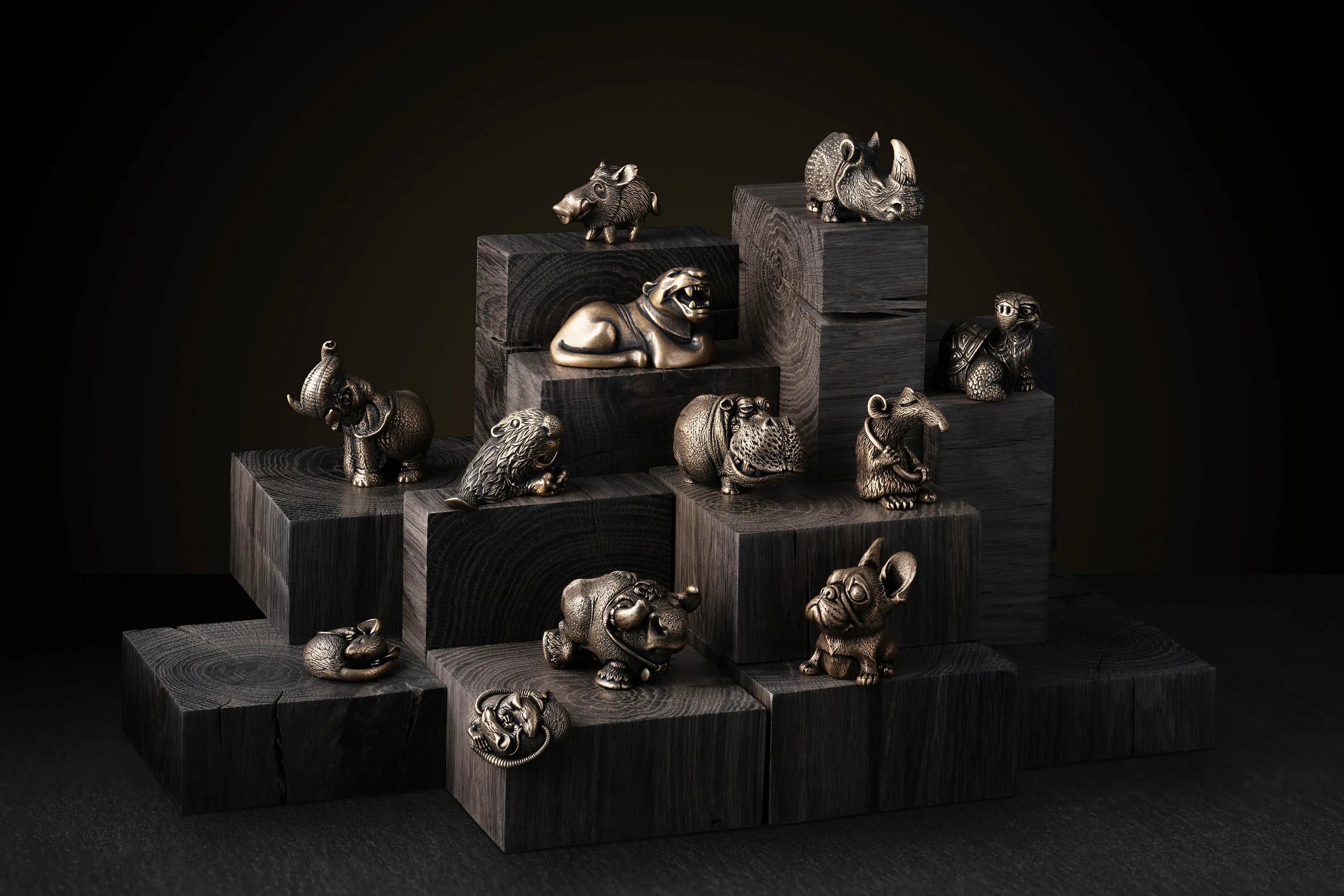 A decorative arrangement of small animal figurines in metallic gold and silver tones displayed on stacked dark wood blocks against a dark studio background.